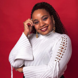 A person in a white sweater poses for a photo in front of a red wall