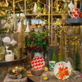 An arrangement of holiday dishware, ornaments, wreathes, and warmly lit home decor