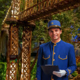 A train conductor in a blue uniform stands beneath a warmly lit model bridge