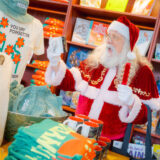 Santa Claus, dressed in red and white, pokes through a shop full of holiday-themed decor