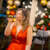 A person in a red dress sings into a microphone on stage