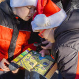 Two children and an adult examine an activity guide featuring a colorful yellow and green map