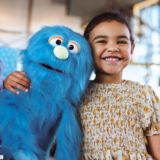 A small child poses for a photo while hugging a blue puppet