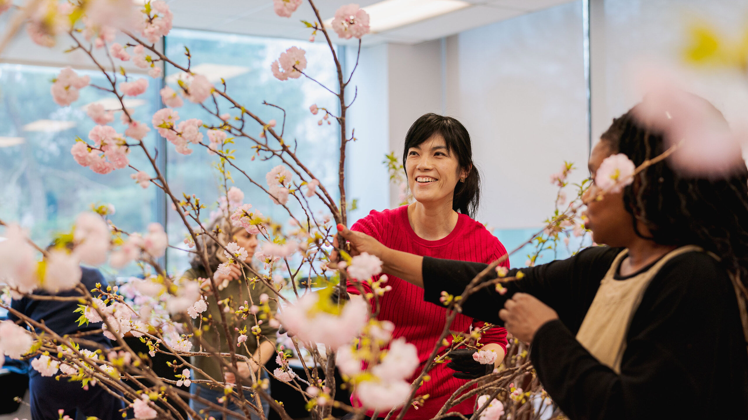 Two people collaborate on a floral arrangement of pink flowers on long branches