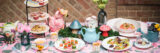 a set-up for afternoon tea features a light blue teapot, towers of desserts and lite bites, and mushroom decor adorn a table in a hot pink printed tablecloth