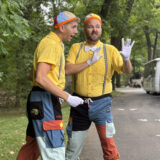 Two people dressed in colorful yellow shirts, patchwork pants, and propeller caps