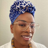 A person in a blue and white headwrap and gold glasses poses for a photo