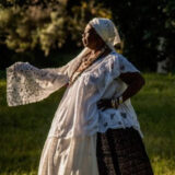 A person in a flowing white dress poses for a photo outdoors at sunset