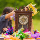 Kids enjoy making hats and crowns on a table of colorful craft materials with a large brown clock