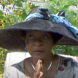 A person in a large black hat with blue ribbons poses outdoors for a photo