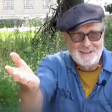 A person in a blue shirt, gray hat, and sunglasses poses for a photo outdoors