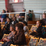 Three people sit in an auditorium to watch a performance.