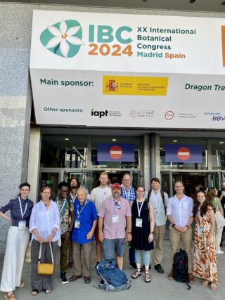 A group of people under a sign for the International Botanical Congress in Madrid, Spain.