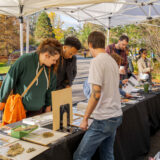 A group of people look at plant specimens and books on a table.