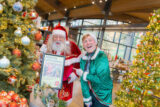 People dressed as Santa and an elf pose among Christmas trees