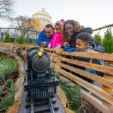 A family of four gets up close with a model train as it passes by on a toy track