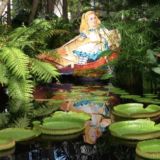 Alice in Wonderland character art in the Enid A. Haupt Conservatory pool with giant water lilies and green plants