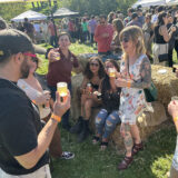 A large group of people enjoys beer and conversation outdoors on a sunny day