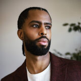 A person in a white shirt and brown blazer poses for a photo