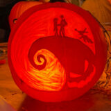 a pumpkin etched with a scene from the Nightmare Before Christmas, with Sally and Jack Skeleton standing on a hill