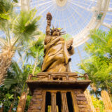 A low view of a model of the Statue of Liberty, with a blue sky visible through the conservatory dome above