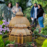 People explore a conservatory space full of miniature buildings made of plant parts