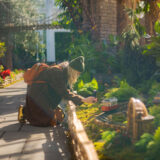 A person kneels down to photograph a model train inside a sunny conservatory space