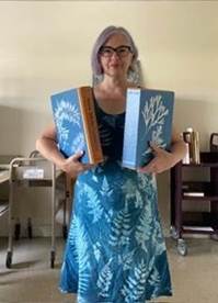 A woman with glasses wearing a blue cyanotype dress holds up two blue books.