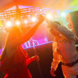 Two people clasp hands while dancing together under green and orange stage lights