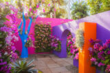 A vivid blue tree grows among walls of flowers in orange, pink, and purple