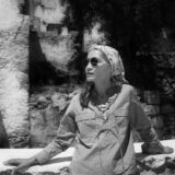 A person wearing sunglasses and a bandana around their head poses for a black and white photo along a cliffside