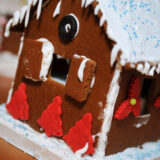 A gingerbread house decorated with white frosting and red "trees"