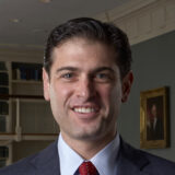 A person in a navy suit and red tie poses for a photo in an office space