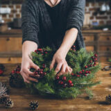 A person makes a wreathe from conifer branches and red berries