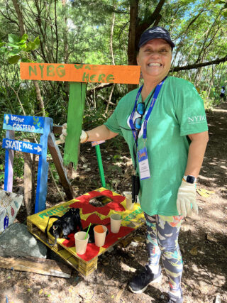 A person in a green shirt poses for a photo with a sign that reads "NYBG WAS HERE"