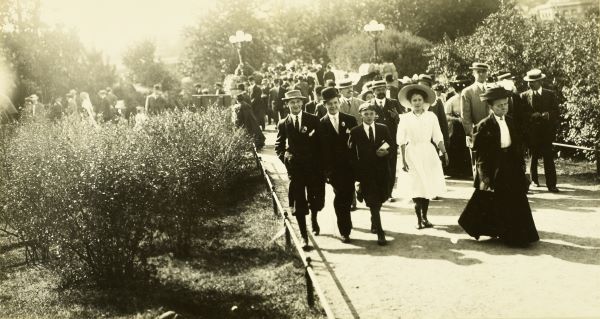 A black and white photo of people in early 20th-century attire entering a garden