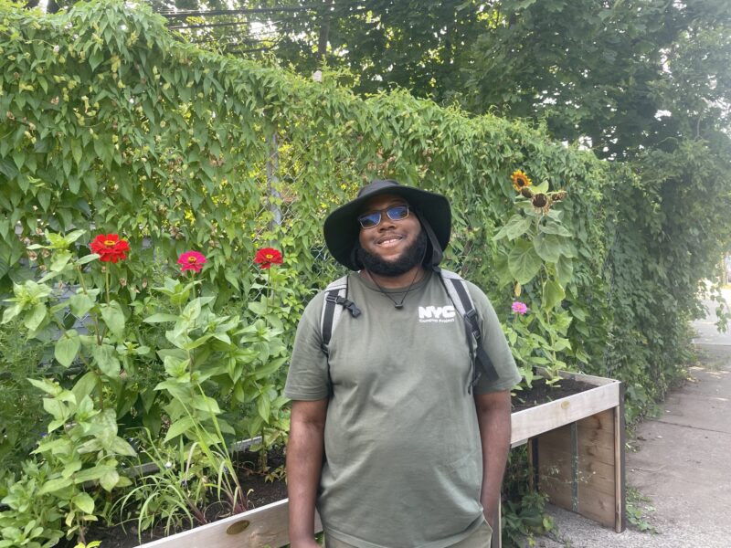 A person in a bucket hat and green shirt poses for a photo in a green garden