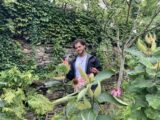 A person poses for a photo among bright green garden foliage