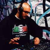 A person in a black sweatshirt bearing the Mexican flag plays music at a DJ table