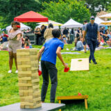 People on a green lawn toss bean bags toward game boards