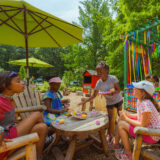 A group of children play make-believe tea party in a sunny outdoor playspace