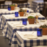 Table settings in a restaurant featuring blue water glasses, white plates, and checkered blue and white tablecloths