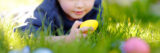 A child lays in the grass, seeking out colorful eggs