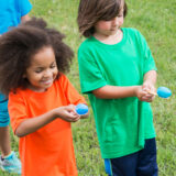 Two children balance colorful eggs on spoons