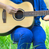 A person in a blue shirt and jeans plays an acoustic guitar outdoors