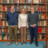 Three people pose for a photo in a library setting