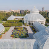 A white glass conservatory surrounding an outdoor pond full of green water lilies and flowers